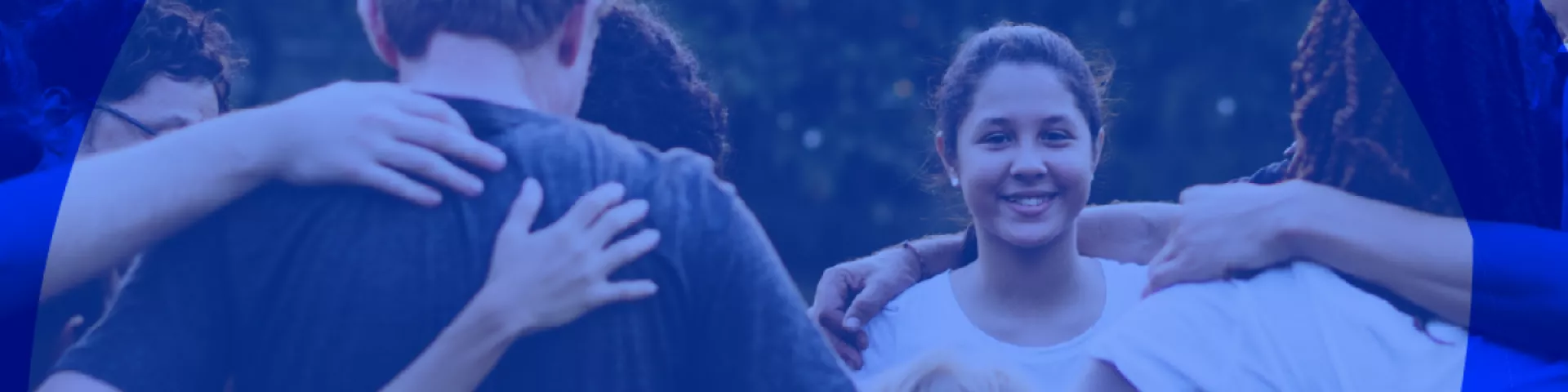 Detail of a girl's face smiling as she embraces other people in a circle of adults and children of different ethnicities.
