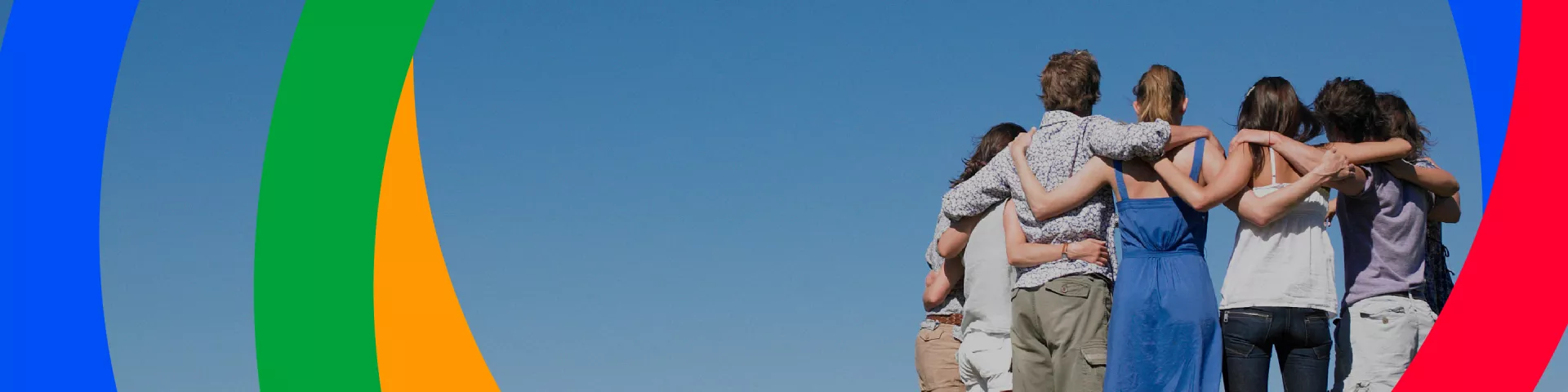 A group of people of different ethnicities, shot from behind, embrace each other as they look towards the horizon.